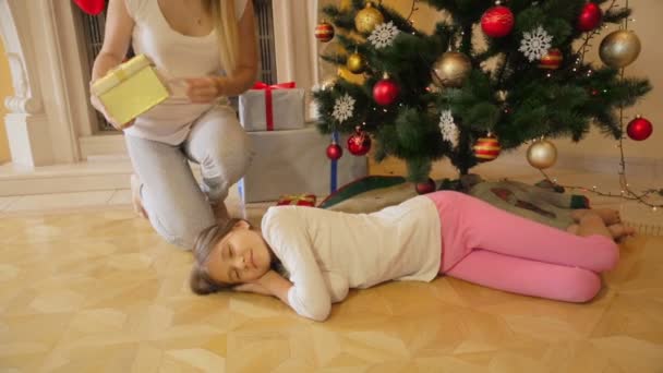 Madre despertando a su hija que se sentía dormida bajo el árbol de Navidad y dándole un regalo. Chica alegre abrazando a la madre — Vídeo de stock