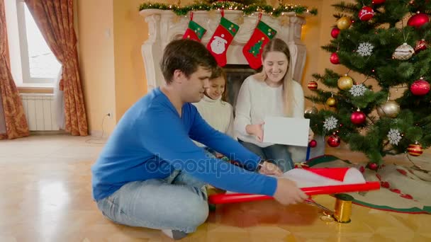 Счастливые улыбающиеся родители с дочерью обертывания подарок на Рождество — стоковое видео