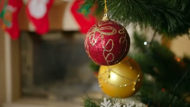 Primer plano de hermosa bola roja colgando y girando en el árbol de Navidad junto a la chimenea decorada — Vídeos de Stock