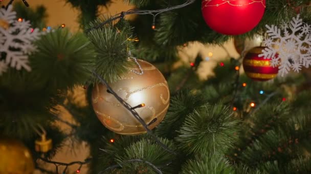 Gros plan de belle boule dorée sur l'arbre de Noël avec des lumières colorées rougeoyantes — Video