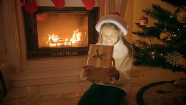 Retrato de menina feliz animado sentado na lareira abre caixa de presente de Natal — Vídeo de Stock