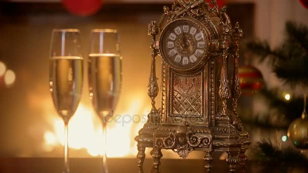 Closeup των δύο ποτήρια σαμπάνιας δίπλα από το παλιό ρολόι που μετράει τα λεπτά για το νέο έτος στο τραπέζι δίπλα στο καίγοντας εστία — Αρχείο Βίντεο