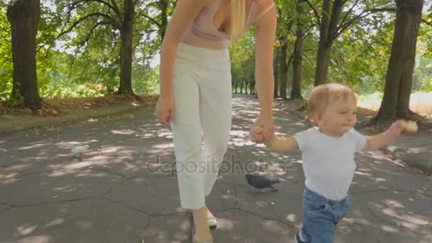 Милый мальчик, гуляющий в парке с матерью и кормящий голубей хлебом — стоковое видео
