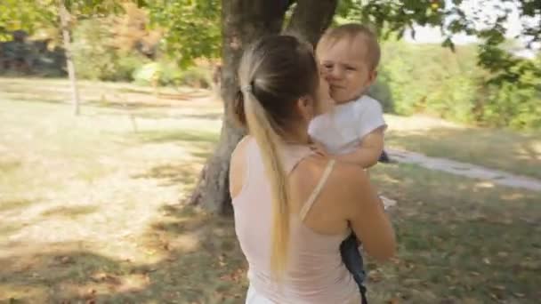 若い女性が公園で彼女の赤ん坊の息子を抱きしめる周りステディカム ショット — ストック動画