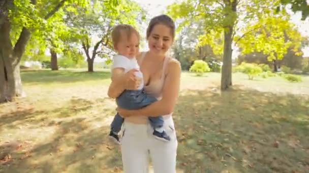 Steadicam-Aufnahme einer glücklichen jungen Mutter, die mit ihrem kleinen Sohn zwischen Bäumen im Park rennt — Stockvideo