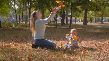Düşen yapraklar ile parkta oynayan bebek oğluyla mutlu genç anne