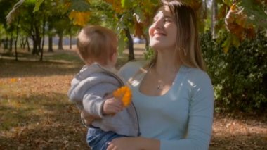 Mutlu genç anne bebek oğlu sonbahar Park ağaç altında sarılma ağır çekim görüntüleri