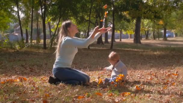 Happy smiling mother with her baby son throwing fallen autumn leaves — Stock Video