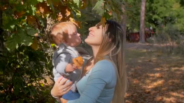 Primo piano filmato al rallentatore di madre felice che abbraccia il suo bambino al parco autunnale — Video Stock