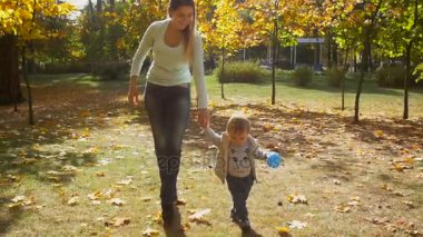 Anne sonbahar Park ile yürüme ve mavi topu tutan güzel bebek çocuk ağır çekim görüntüleri