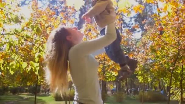 Медленный кадр веселой молодой матери, обнимающей и воспитывающей своего маленького сына в парке в яркий солнечный день — стоковое видео