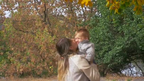 Imágenes de primer plano 4K de feliz madre joven abrazando y lanzando aquí bebé hijo en el parque de otoño — Vídeos de Stock