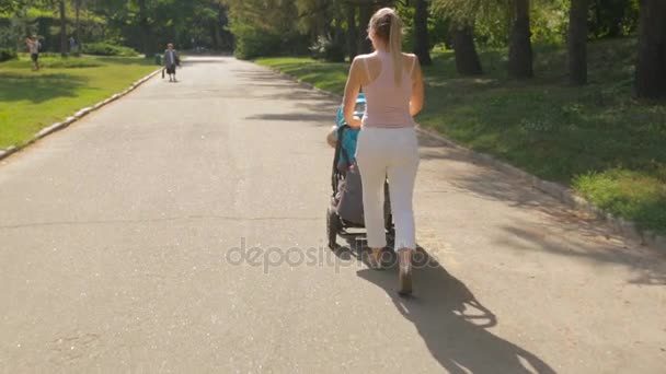 Vacker ung kvinna promenader med barnvagn på sommaren park — Stockvideo
