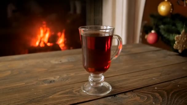 Closeup vídeo em câmera lenta de xícara de chá, lareira em chamas e árvore de Natal decorada — Vídeo de Stock