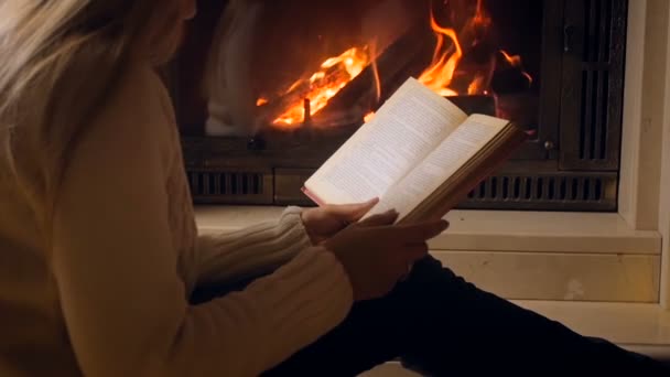Slow motion video av woma bok som sitter på golvet bredvid brinnande eldstad i huset på natten — Stockvideo