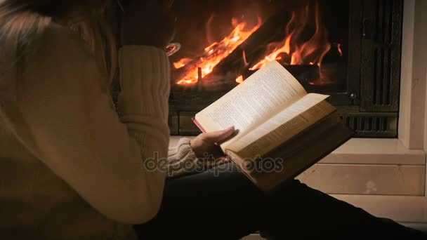 Slow motion video of woman sitting by the fireplace, reading book and drinking tea — Stock Video