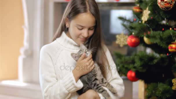 4k close seup footage of happy smiling girl hugging and caressing cute kitten next to Christmas tree at living room — стоковое видео