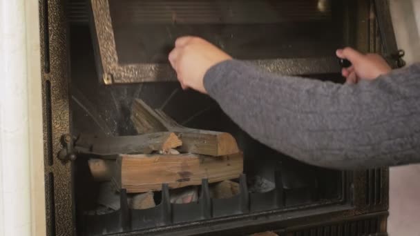 若い男の 4 k 映像暖炉のドアを開き、内部の木の丸太を置く — ストック動画