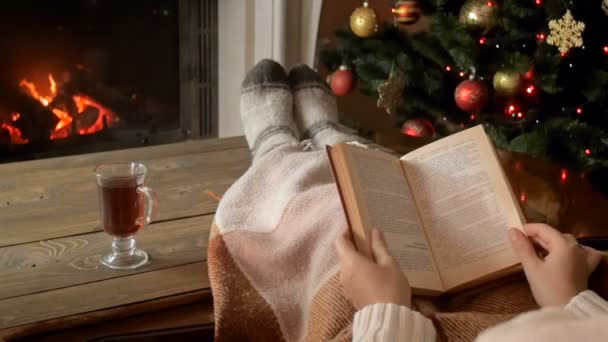 Closeup slow motion footage of woman reading book next to Christmas tree and burning fireplace — Stock Video