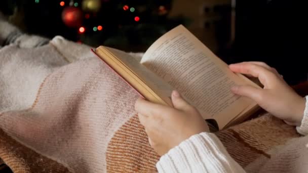 Closeup slow-motion video van vrouw liggend onder plaid naast kerstboom en lezen van boek — Stockvideo