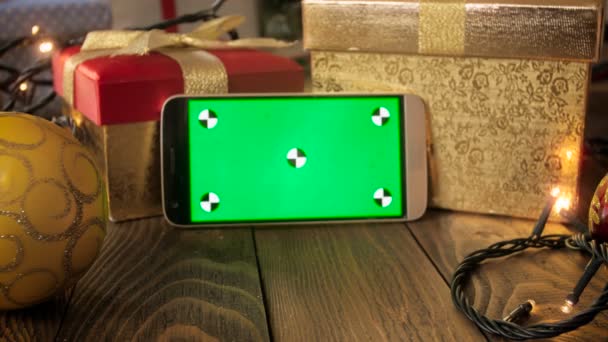 Крупный план 4k съемки мобильного телефона с зеленым экраном на деревянном столе, украшенном на Рождество — стоковое видео