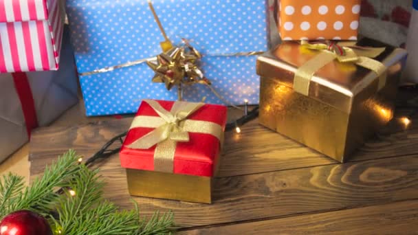 4 k video van vele vakken met giften, Kerstverlichting en kleurrijke kerstballen op houten tafel — Stockvideo