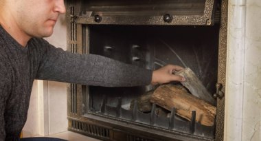 Closeup image of young man throwing wood in fireplace clipart