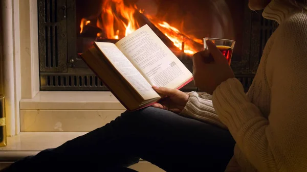 Imagen de primer plano de la joven sentada junto a la chimenea con libro —  Fotos de Stock