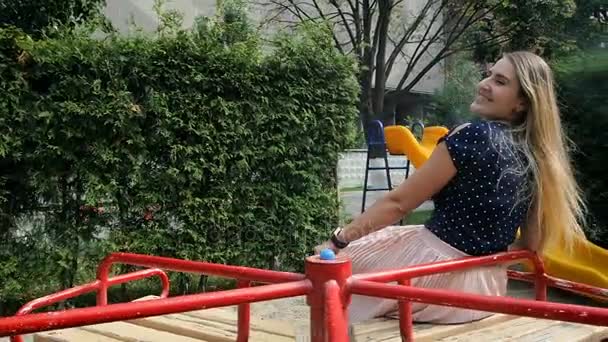 Медленная съемка красивой улыбающейся молодой женщины, катающейся на карусели на детской площадке в солнечный летний день — стоковое видео