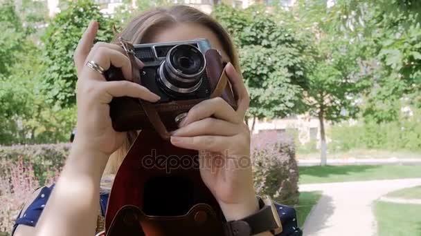 Closeup slow motion footage of young woman making photo on old manual camera at park — Stock Video