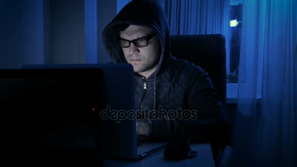 Felvétel a fiatal férfi kapucnis pulcsi és szemüvegek számítógépen dolgozik rajta. Fogalmának programist vagy hacker — Stock videók