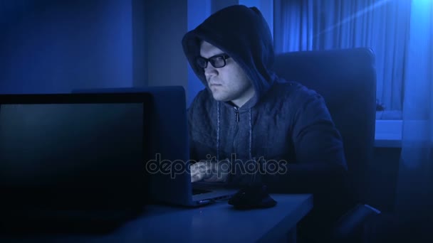 Filmaufnahmen eines jungen Mannes mit Kapuzenpulli und Brille, der nachts am Computer arbeitet — Stockvideo