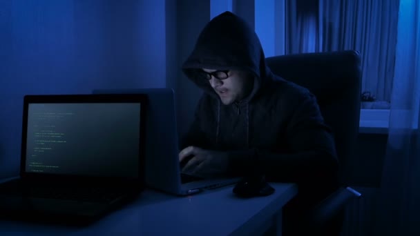 Graciosas imágenes de 4k de hombres con capucha en la habitación oscura finge ser hacker. El hombre que trabaja en el ordenador portátil por la noche — Vídeos de Stock