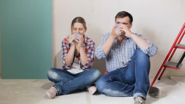 4k imagens de feliz jovem casal apaixonado ter pausa no chão e beber chá no novo apartamento — Vídeo de Stock