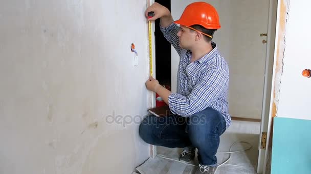 Filmación del joven manitas en la pared de medición hardhat con cinta métrica — Vídeos de Stock