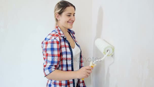 Slow motion beelden van prachtig lachende vrouw schilderij wanden met een verfroller op Nieuw appartement — Stockvideo