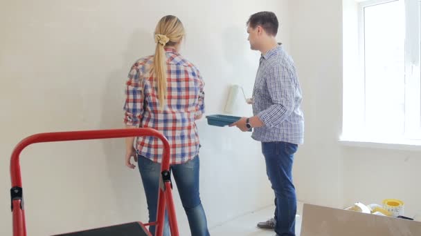 Slow motion footage of young man with wife painting walls with paint roller at new house — Stock Video