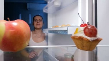 Kırmızı elma pasta yerine buzdolabından geceleri alarak aç genç kadın 4 k görüntüleri. Diyet kavramı