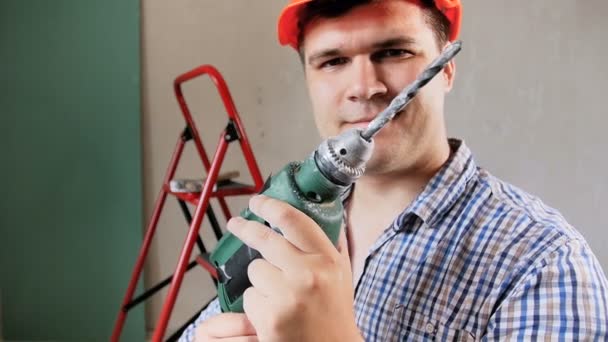 Slow motion bilder av unga förman i hardhat använder elektriska borra på hus under renovering — Stockvideo