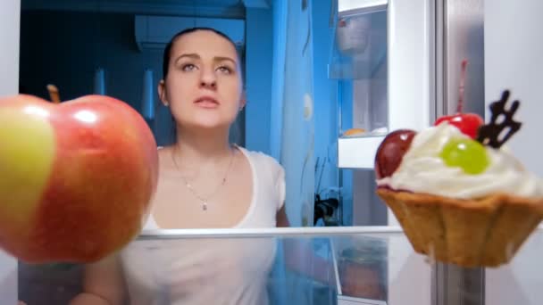 4 k felvétel, fiatal nő keres valamit enni éjszakánként és figyelembe friss Alma a hűtőből — Stock videók