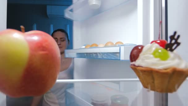 Imágenes de 4k de una mujer joven tomando manzana fresca de la nevera por la noche. Perfecto para una alimentación y una dieta saludables — Vídeos de Stock