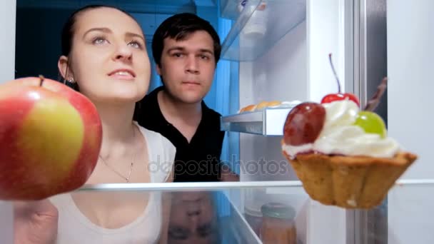 4 k felvételeket a fiatal pár éjjel, és hűtőben élelmet kapott éhes. Koncepció a fogyókúra — Stock videók