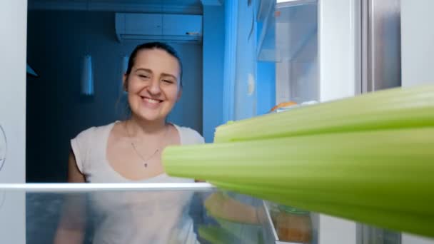 Images 4k d'une heureuse femme souriante prenant du céleri du réfrigérateur la nuit. Concept de régime — Video