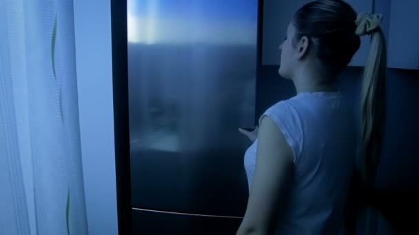 Slow motion beelden van jonge slaperig vrouw nemen van voedsel uit koelkast bij nacht — Stockvideo
