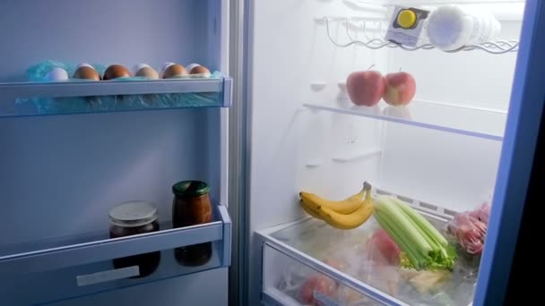 Imágenes panorámicas del refrigerador abierto lleno de comida por la noche — Vídeos de Stock