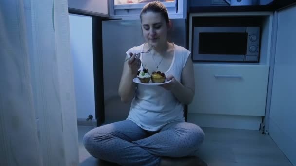 Slow motion video av ung kvinna i pyjamas äta kakan på natten — Stockvideo