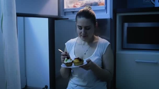 Slow motion video av hungrig kvinna äta kakan nära kylskåp på natten — Stockvideo