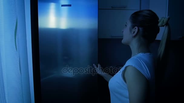 Vídeo en cámara lenta de una hermosa mujer joven tomando manzana fresca del refrigerador por la noche. Concepto de nutrición saludable y dieta — Vídeo de stock