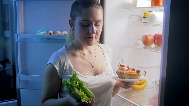Slow motion video of young woman choosing between vegetables and cake for late dinner — Stock Video