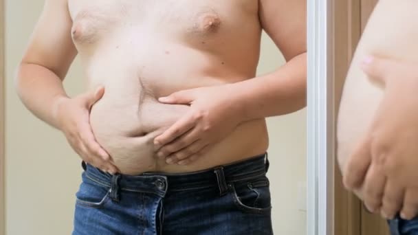 Imágenes de 4k del hombre con sobrepeso parado en el espejo y fingiendo estar en forma y musculoso — Vídeos de Stock